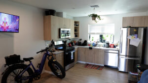 An interior photo of a room at The Ranch House in Nevada County, with a kitchen, full sized refrigerator, wood floors, a television, light coming in the window, and a bicycle parked inside.