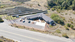 An overhead photo of The Ranch House shows a v-shaped building with a parking area, solar panels in a field beside it, and grass and trees behind it. 